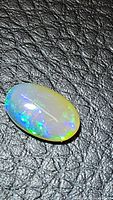 Close-up photo of oval Ethiopian opal showing play of color in blue and green with translucent base on textured black background