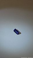 Octagon cut natural tanzanite gemstone placed on a plain surface showing the cut and color.