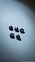 Five individual loose blue sapphire gemstones arranged in a small cluster on a white background with light and shadow play slightly enhancing their blue color.