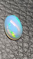 Close-up image of an oval cabochon cut Ethiopian opal showing white translucent body and bright green, yellow, and blue color flashes.