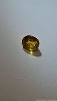 Natural oval cut canary yellow sapphire gemstone resting on white surface, showing bright yellow color and internal clarity.
