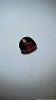 Photo of a single pear cut natural red spinel gemstone showing deep red color and reflective surface on a plain background.