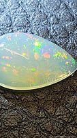 Close-up visual of pear-shaped, 14x9mm Ethiopian opal showing vivid multicolored play-of-color against black textured background.