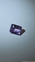 Natural pink purple amethyst gemstone in emerald cut shown against white background highlighting transparency, color and cut details.