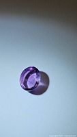 Photo of a deep purple oval cabochon amethyst gemstone on a neutral background with light casting a shadow