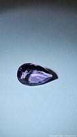 Photo of a pear-shaped natural purple amethyst gemstone viewed from top angle showing rich color and faceting.