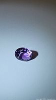 Oval cut deep purple amethyst gemstone on a white background showing its brilliant facets.