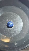 Round cabochon natural blue star sapphire with visible six-rayed star effect under light in dark setting.