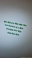 Multiple natural Colombian emeralds arranged on a white background, showing shape, size, and color uniformity