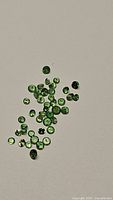 Loose calibrated natural tsavorite garnet gemstones in varying shades of green, spread out on neutral background.