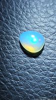 Pear-shaped natural Ethiopian opal cabochon gemstone showing vibrant blue, purple, and green color flashes on black textured background.