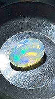 Close-up of faceted oval Ethiopian opal with visible flashes of green, blue, and yellow colors under lighting.