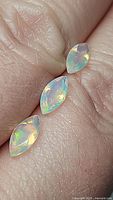 Three marquis cut natural Ethiopian opals on a fingertip, showing colorful play of light and transparency.