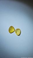 Photo of two natural yellow sapphire gemstones on a white background, showing their shape and color.