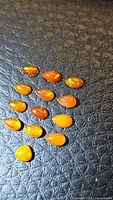 Overhead photo showing all 13 pear-shaped fire opal cabochons arranged on textured black surface, highlighting varying intensity of orange and flashes.