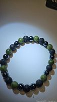 Photo of bracelet arranged flat showing alternating pattern of green jade, hematite and black lava beads under light.