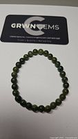 Green jade bead bracelet arranged in a circle on a white background with GRWN GEMS card in background.
