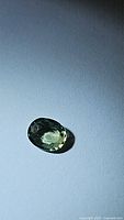Top-down photo of the oval cut green sapphire showing facets and color.