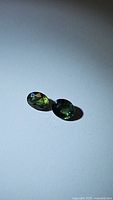 Two oval cut green sapphires displayed on white background, showing color and facets