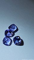 Four cushion cut deep blue tanzanite gemstones placed on a white surface, showing their color and cut.