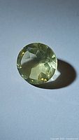 Close-up image of a round cut natural lemon citrine gemstone displaying its transparent pale yellow-green color and faceted cut.