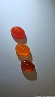 Three polished carnelian cabochon gemstones arranged vertically on a white background, showing rich translucent orange shades and glossy smooth surfaces.