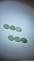 Six oval cabochon mint green kyanite gemstones arranged in two rows on a white background under focused light showing their color and translucency.