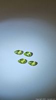 Four natural pear cut apple green peridot gemstones arranged on white background under light, showing their color and clarity.