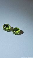 Pair of natural apple green peridot round faceted gemstones, showing vibrant green color and clarity.