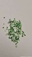 Photo of scattered small green round faceted tsavorite garnet gemstones on a plain surface, showcasing size and color.