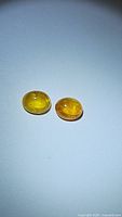Two deep yellow oval cabochon sapphires side by side photographed on plain background