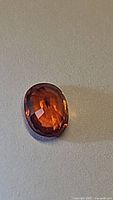 Close-up front view of the oval cut orange spessartite garnet gemstone showing facets and color.