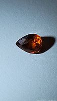 Close-up of pear cut natural spessartite garnet gemstone with vibrant orange color on light background.