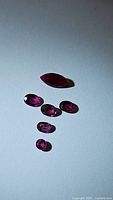 Six natural untreated rubies on white background, one marquise-shaped and five oval-shaped stones, photographed from above.