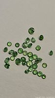 Image showing multiple small round cut green tsavorite garnet gemstones scattered on a white background.