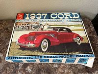 Photo of the unopened or partially opened model car kit box featuring an illustration of a red 1937 Cord 812 Convertible Coupe car with black convertible top.