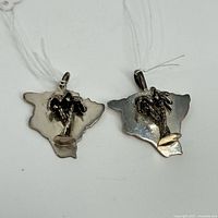 Photo showing both silver Hawaii-shaped pendants with palm tree embellishments from the back side