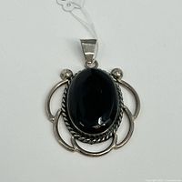 Front view of the sterling silver pendant with polished oval black onyx set in decorative open silver frame with rope detailing.
