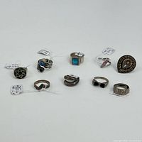 Top view photo showing all nine sterling rings arranged in rows, showcasing various stone types and designs including colored stones and engraved bands.