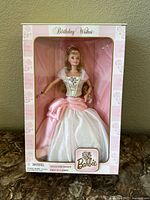 Front view of Barbie doll in original box showing the doll dressed in pink and white birthday-themed gown with floral decoration.