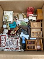 Box containing various miniature dollhouse furniture and accessories including chairs, cabinets, rugs, mirrors, and small decor items.