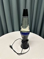 Full view of the clear lava lamp with black base and cap, showing electric cord wrapped around base.