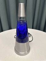 Full view of dark blue lava lamp with silver base and electrical cord on round table with light background.