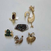 Overview of six assorted animal and figural brooches arranged on a white background.