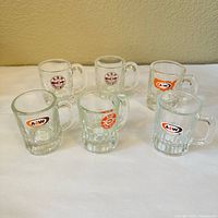 Group of six clear glass handled mugs with assorted A&W logos on front