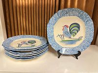 Group of 8 stacked blue and white plates with rooster design, one plate displayed upright on stand