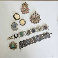 Full view of the vintage jewelry group including pins, brooches, bracelets, and clip-on earrings arranged on white background.