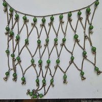 Full view of the green bead and metal chain necklace showing the zigzag chain pattern punctuated with green beads and small dangling metal elements at chain ends.