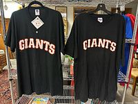 Pair of black Giants T-Shirts on hangers on a metal shelf, one with buttons and one without
