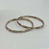 Pair of two sterling silver bangles with embossed sea designs and visible patina, arranged overlapping on a white background